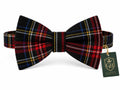 A pre-tied bow tie in a red, black, and blue tartan plaid pattern, shown with a green brand tag on a white background.
