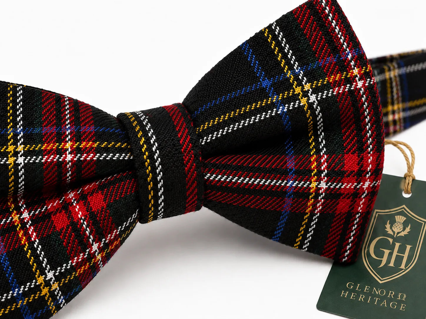 A black plaid bow tie with red, blue, yellow, and white stripes, featuring a green 'Glenorn Heritage' brand tag on a white background.