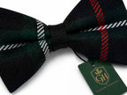 A dark green and black plaid bow tie with red and white stripe details, tied with a black ribbon and featuring a green 'Glenor Heritage' brand tag.