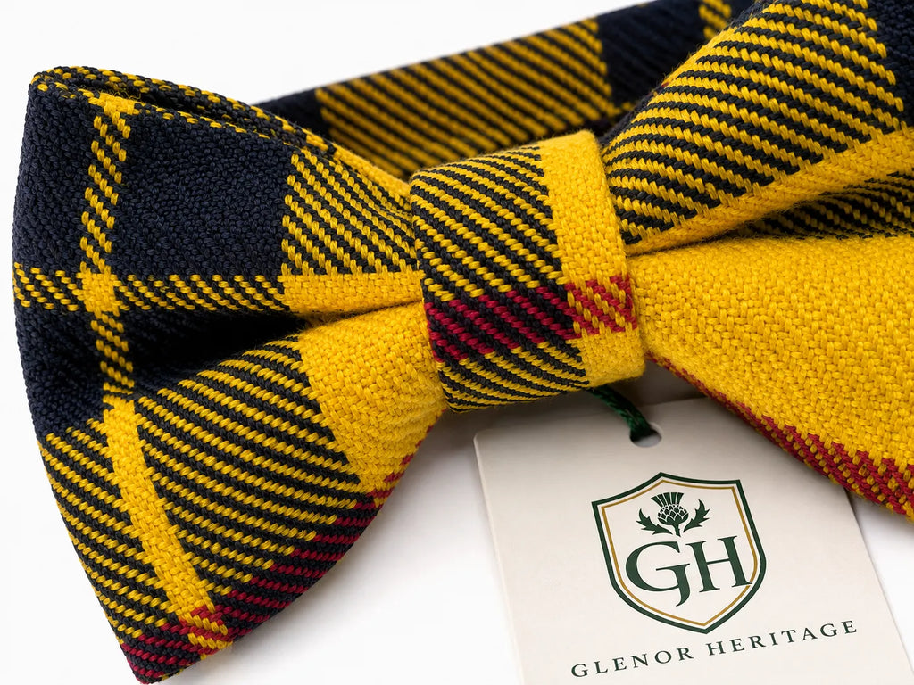 A pre-tied bow tie in a yellow, navy, and burgundy tartan pattern, shown with its white Glenor Heritage brand tag on a clean white background.