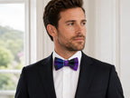 A man wearing a black suit jacket, white dress shirt, and a purple and blue patterned bow tie, shown in a bright indoor setting.